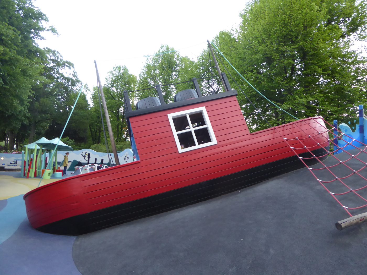 A large red wooden boat run aground as a climbing structure in a public garden